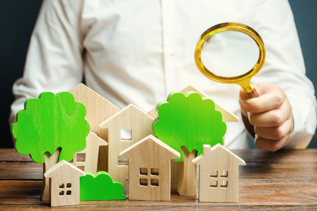 Ein Mann hält eine Lupe über Holzhäusern und Bäumen. Immobilienbewertung und -auswahl